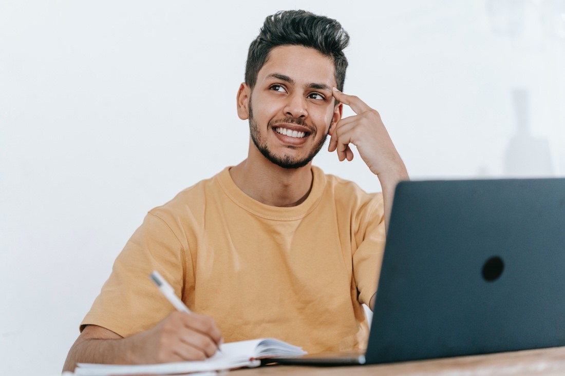 A young man looks up from his studies, which include a laptop and notebook. He’s utilizing a high-speed Internet connection thanks to the Affordable Connectivity Program.